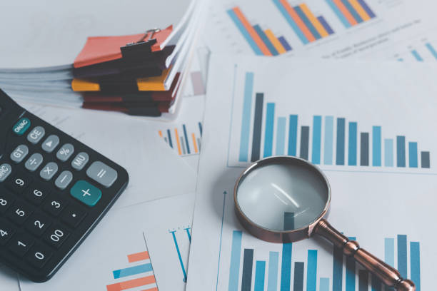 istock magnifying glass calculator and business statistical chart reports All laying on the table ,Financial document management and marketing Annual budget account updates company growth information 1456714709