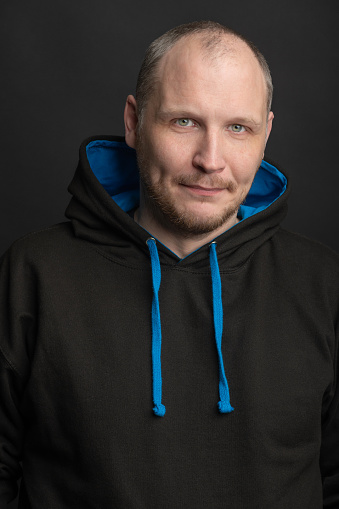 Lifestyle and fashion concept. Close-up man studio portrait. Model wearing black hoodie sweatshirt with blue laces and copy space. Black studio background. Man looking at camera
