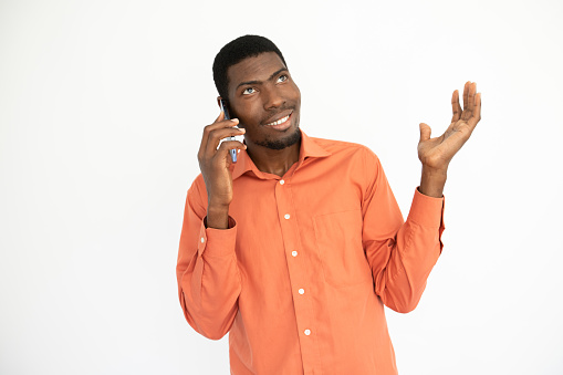 Portrait of happy young man having conversation on mobile phone. African American guy wearing orange shirt talking on smartphone. Mobile communication concept
