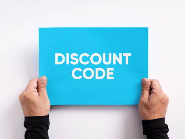 istock Discount code offered to customers as a purchasing incentive that reduces the price of an order. Male hand holding a blue paper with the message discount code. 1456725229