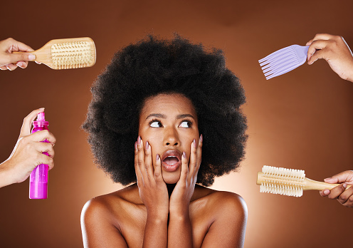 Mujer negra pensando en el cuidado del cabello, herramientas para afro natural y toma de decisiones de productos de belleza. Chica africana sorprendida con opciones, cepillos de salón y laca para el cabello en el estudio con fondo marrón oscuro photo