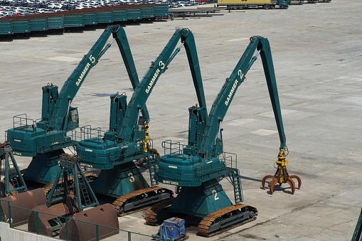 Barcelona, Spain - 08 06 2022: Tree green tracked excavators form Mantsinen company use for handling of scrap are parked in port, awaiting loading and discharging scrap form ships in cargo terminal.