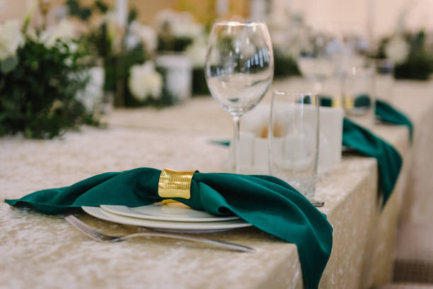 istock Wedding set up, dinner table reception. Table setting. A plate with a green cloth towel and knives and forks, and glasses. Flower composition with eucalyptus leaves and candles in center of the table. 1456736917
