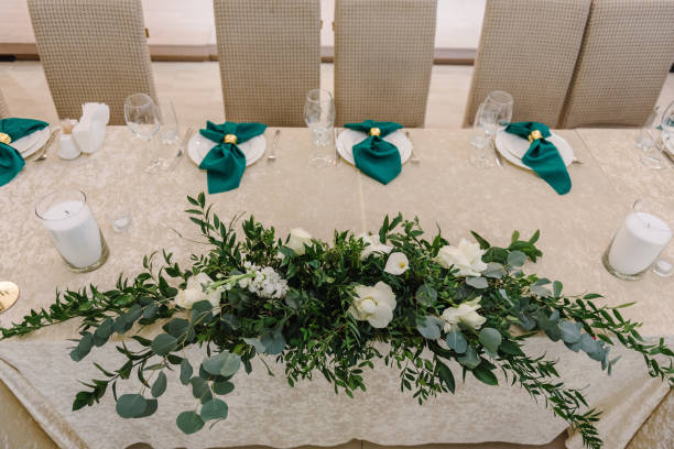 istock Wedding set up, dinner table reception. Flower composition with eucalyptus leaves and candles in center of the table. A plate with a green cloth towel, knives and forks next to the plate.  Top view. 1456739917