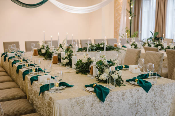 Wedding dinner table reception. A plate with a green cloth towel, knives and forks next to the plate. Flower composition with eucalyptus leaves in the center of the table and burning candles. Closeup.