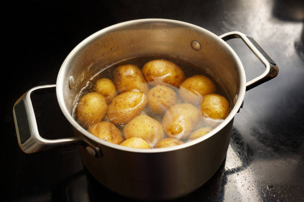 Potatoes with peel in a stainless steel pot with boiling water on the stove, healthy cooking concept, copy space, selected focus stock photo