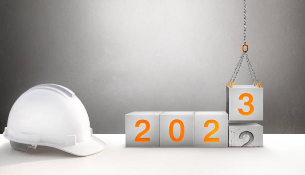 istock Happy New Year 2023 Construction and Industry. White Helmet and a numbered concrete cube on the desk of an engineer or construction worker. building with Cranes construction concept. 1456740357