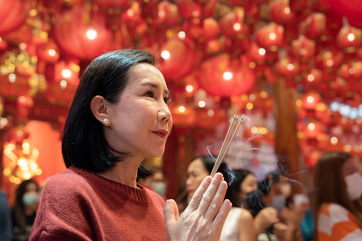 Asian mother and daughter lighting incense and praying the god together at shrine on Chinese New Year holiday.