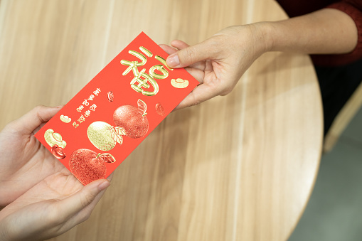 Close up of hand of an Asian Chinese woman giving red envelope to her relative during Chinese New Year celebration