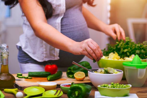 Healthy pregnancy concept Happy pregnant woman cooking at home, doing fresh green salad, eating many different vegetables during pregnancy, healthy pregnancy concept olivia mum stock pictures, royalty-free photos & images