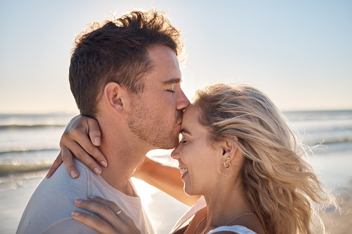 Love, dating and couple kiss at beach enjoying romantic holiday, vacation and honeymoon by ocean. Happiness, summer and young man and woman embrace, show affection and bonding together in nature