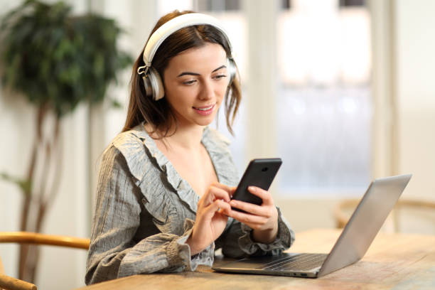 istock Woman with headphones using laptop checking phone 1456747393