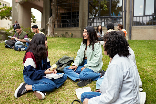 Focus on foreground group of women in teens and 20s sitting on grass and enjoying a break from class. Property release attached.