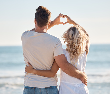 Love, heart and hands of couple at beach for travel destination, happy and summer break. Nature, trust and wellness with man and woman bonding by ocean shoreline for support, peace and adventure