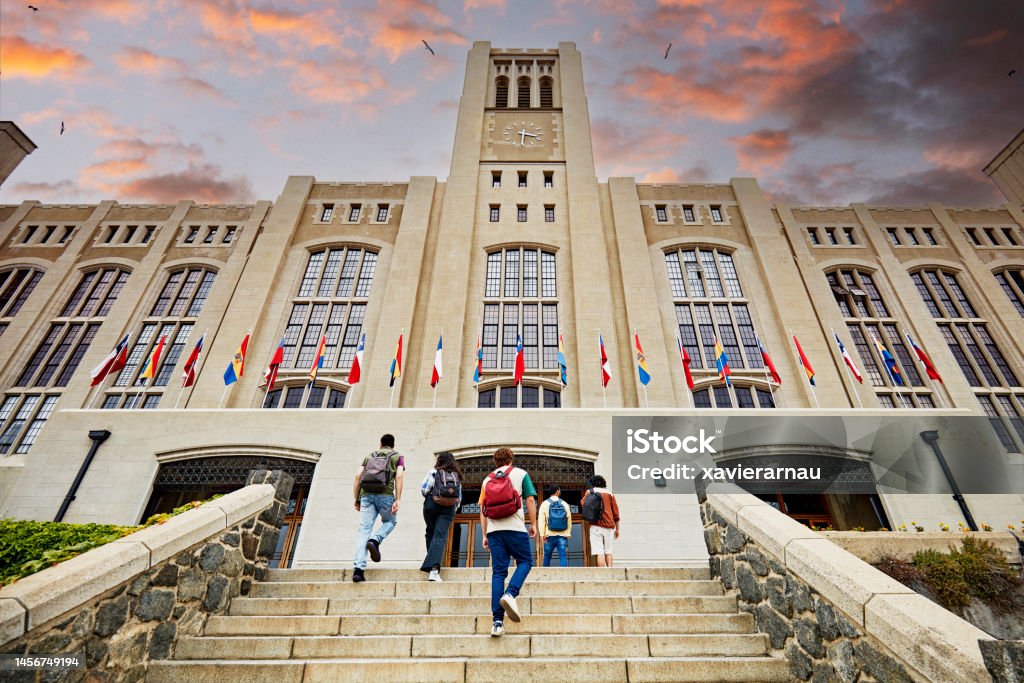 College students arriving for night school Low angle view of men and women with backpacks walking up staircase to building entrance with dramatic sunset sky overhead. Property release attached. Campus Stock Photo