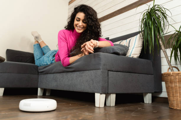 istock Woman relaxing on the sofa and turning on smart vacuum cleaner 1456750849
