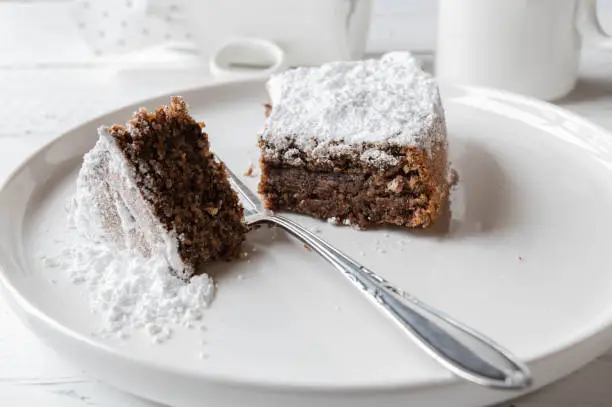 Delicious italian chocolate almond cake. Baked with real dark chocolate and grated almonds. Served with powdered sugar topping on a white plate with fork on white table background. Closeup and front view