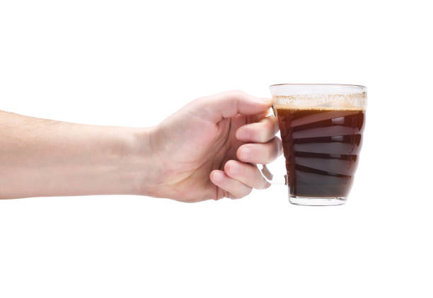 A man's hand holds a glass mug with warm coffee on a white background.
