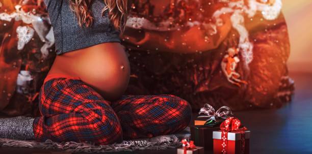 Happy pregnant woman at Christmas eve Happy pregnant woman at Christmas eve sitting on the floor in the decorated room at home and preparing to open Christmas gifts, new life as the best present for Xmas holidays olivia mum stock pictures, royalty-free photos & images