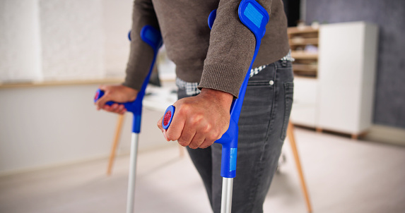 Worker With Crutches At Workplace Or Office. Rehabilitation Benefits