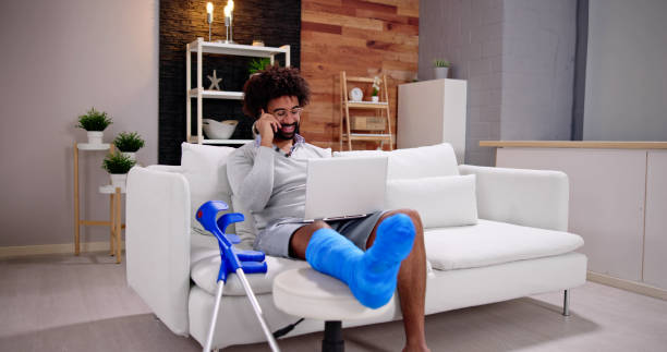 istock Happy Young Man With Broken Leg Sitting On Sofa Talking 1456759307
