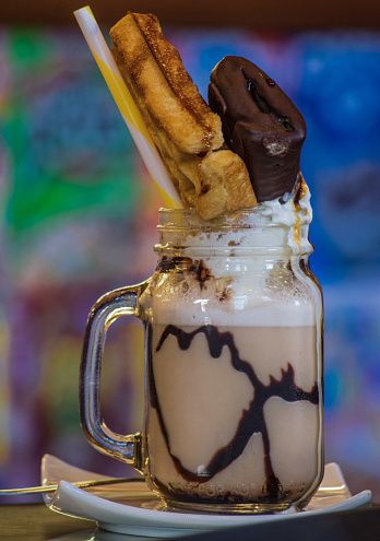 Chocolate milkshake in a glass cup topped with cream and a straw
