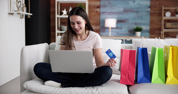 Young Woman Sitting On Sofa Shopping Online With Shopping Bags.