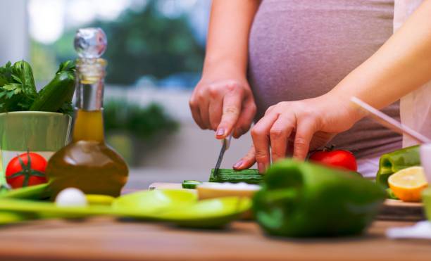 Organic nutrition for pregnant woman Pregnant female cutting fresh vegetables for salad at home, body part, vitamins and organic food for future mother, healthy lifestyle in pregnancy period olivia mum stock pictures, royalty-free photos & images
