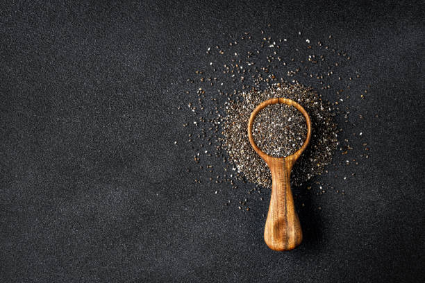 top view of chia seeds in round wooden scoop on black background stock photo