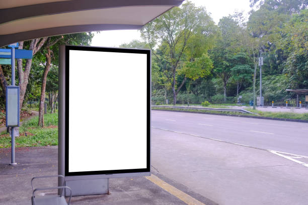 istock Blank advertising poster banner mockup template at empty bus stop shelter by main road. Greenery around vertical out-of-home OOH billboard advertising display space. 1456766775