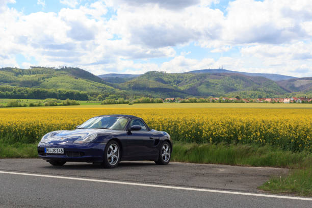 panorama con roadster convertible deportivo azul porsche boxster 986 frente al campo de colza y la montaña brocken en harz, alemania - germany landscape nissan roadster fotografías e imágenes de stock