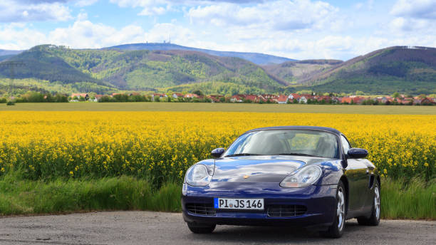 panorama z niebieskim samochodem sportowym kabriolet roadster porsche boxster 986 przed polem rzepaku i górą brocken w harzu, niemcy - germany landscape nissan roadster zdjęcia i obrazy z banku zdjęć