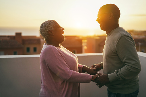 Senior african couple dancing outdoors with sunset on background - Focus on