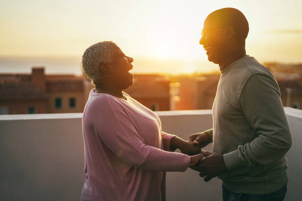 Senior african couple dancing outdoors with sunset on background - Focus on stock photo