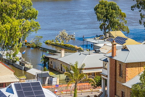 High angle view looking down on flooded historic houses and buildings in Randell Street, Mannum, South Australia. Temporary earthen levee has controversially left some properties on river side to be inundated with muddy floodwater. Backyards are flooded and houses threatened.  An Australian national flag flutters in the breeze from a backyard. Solar panels installed on roofs. Jan 12, 2023