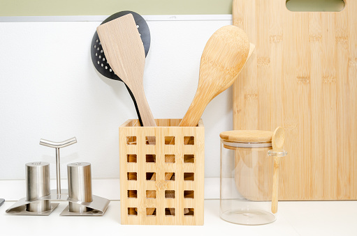 Eco friendly Bamboo kitchen utensils on kitchen table. wooden and plastic spatulas for cooking on background of cutting board in kitchen close up.