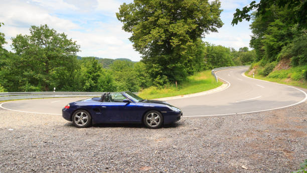 niebieski roadster porsche boxster 986 na ulicy z zakrętem w hunsrück. samochód jest dwumiejscowym samochodem sportowym z centralnie umieszczonym silnikiem produkowanym przez niemiecką firmę motoryzacyjną porsche. - germany landscape nissan roadster zdjęcia i obrazy z banku zdjęć