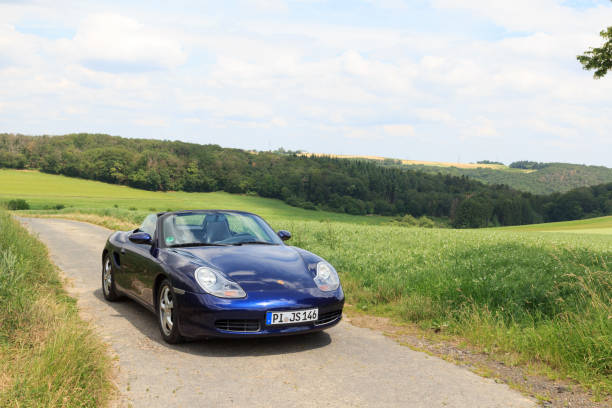 roadster azul porsche boxster 986 con panorama de montaña de hunsrück. el automóvil es un automóvil deportivo biplaza de motor central fabricado por la compañía automotriz alemana porsche. - germany landscape nissan roadster fotografías e imágenes de stock