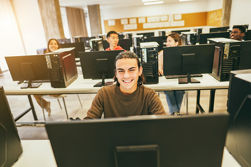 Young students using computers inside technology class at school room - Focus on center guy face