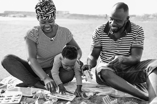 African parents and little son having fun with wood toys on the beach - Focus on father face - Black and white editing