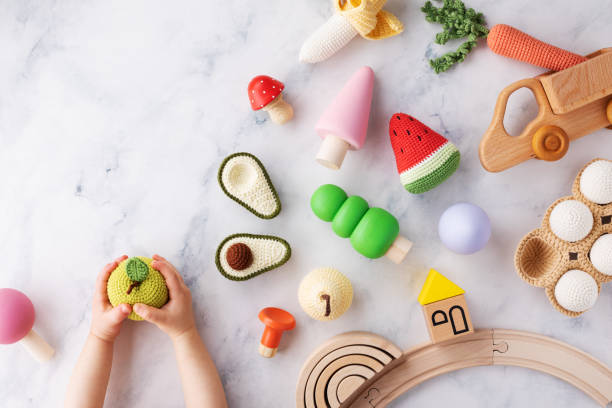 Baby hands with cute wooden and knitting eco toys for activity, motor and sensory development on table top view. stock photo