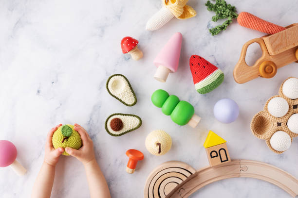 Baby hands with cute wooden and knitting eco toys for activity, motor and sensory development on table top view. Baby hands with cute wooden and knitting craft eco toys for activity, motor and sensory development on table top view. green toy stock pictures, royalty-free photos & images