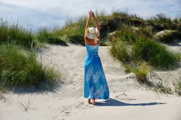 Young slim girl on the beach in Denmark on a sunny day. A girl in a long blue flowing dress on the Hirtshals beach in Denmark. Elegant young girl in a hat and dress on the beach.