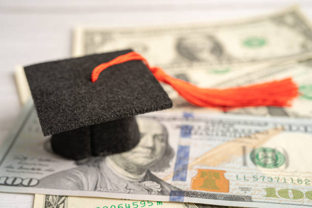 istock Graduation gap hat on US dollar banknotes money, Education study fee learning teach concept. 1456788256