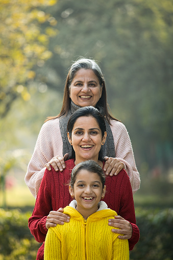 Three generations of cheerful females having standing one by one behind each other at park