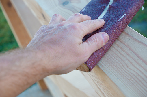 Sanding wood. A male carpenter is sanding the wooden beams of a made gazebo. Hand of a Carpenter Rubbing Wood With Sand Paper