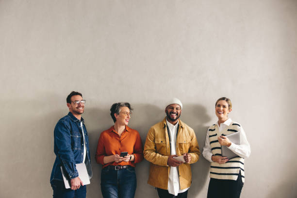 Cheerful job applicants standing in a waiting area Cheerful businesspeople smiling happily while waiting in line for an interview. Group of shortlisted job applicants holding different digital devices in a modern office. casual job interview stock pictures, royalty-free photos & images