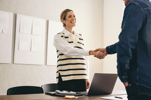 Excited businesswoman shaking hands with her new business partner. Happy businesswoman hiring a successful job candidate. Cheerful businesswoman closing a new deal in her office.