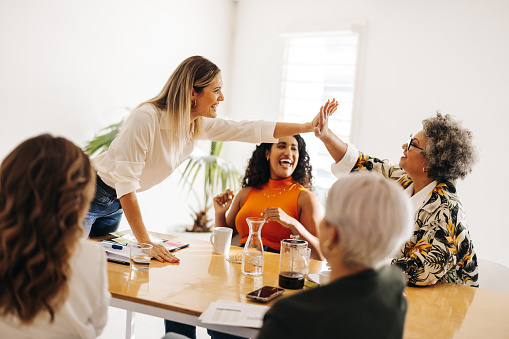 Business colleagues high fiving each other during a meeting in a boardroom. Successful businesswomen celebrating their achievement. Diverse businesswomen working together in an all-female startup.