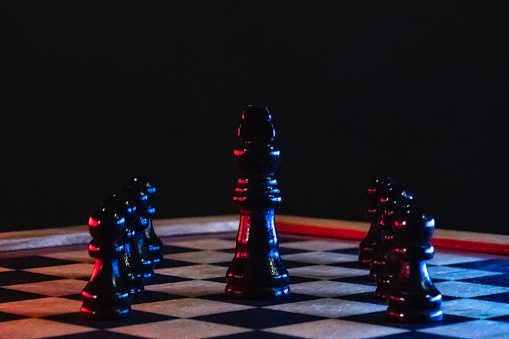 Chess Pieces on Wooden Chess Board with Black Background and Blue and Red Highlights